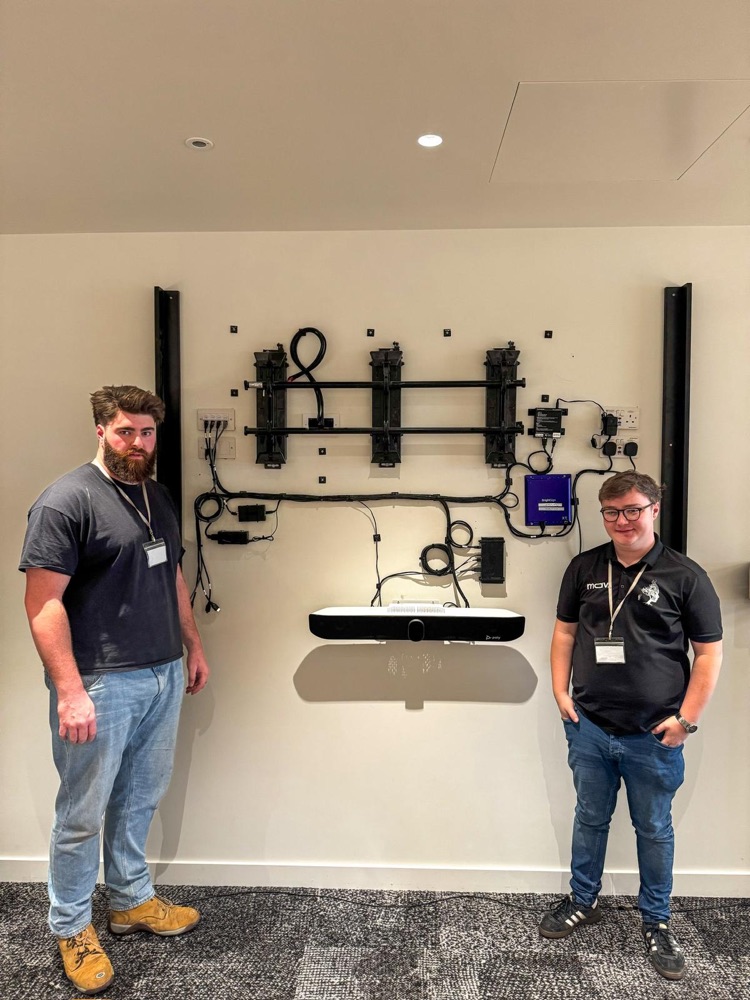 Two MAV engineers beside a wall-mounted video wall mounting rig and Poly video bar during a London office installation
