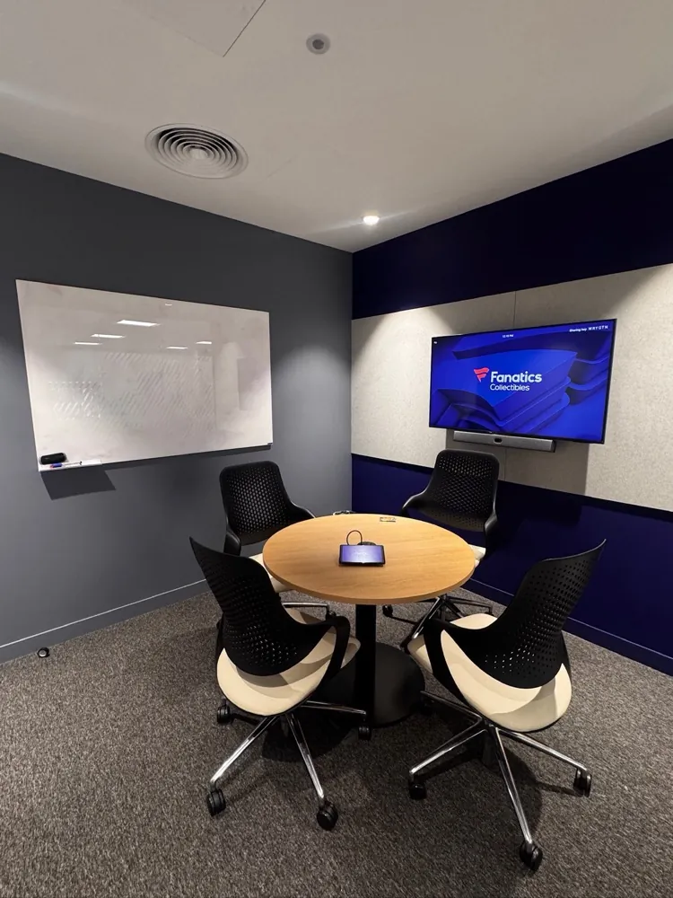 Four-person huddle room with a round table, whiteboard and video conferencing display