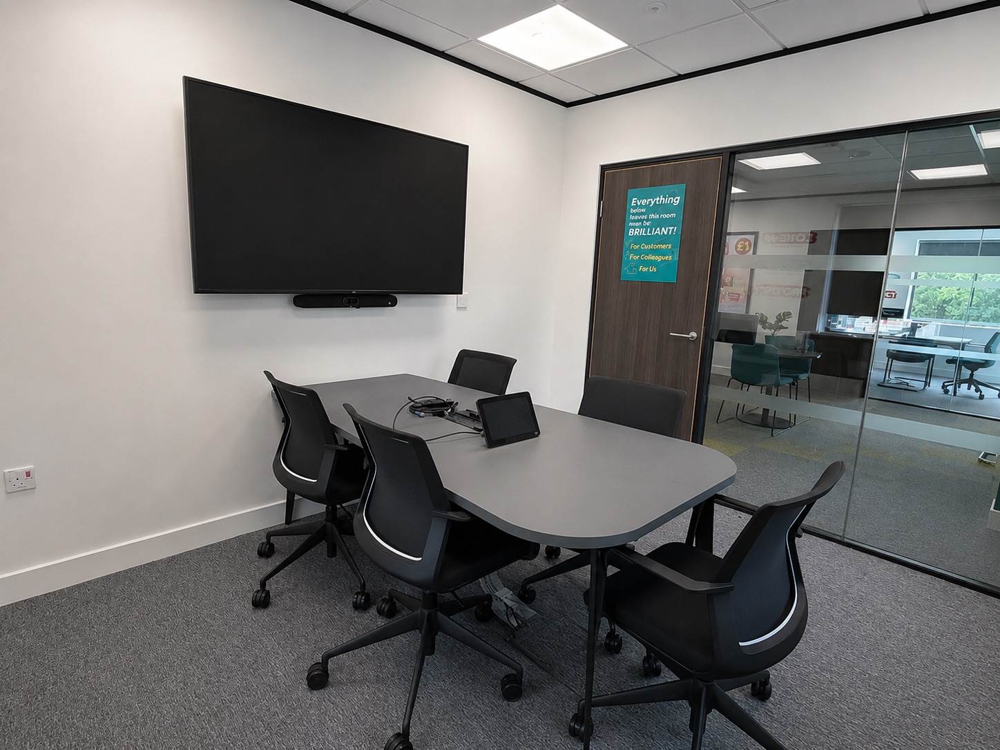 Small meeting room with a wall-mounted display, video conferencing bar and tabletop touch controller