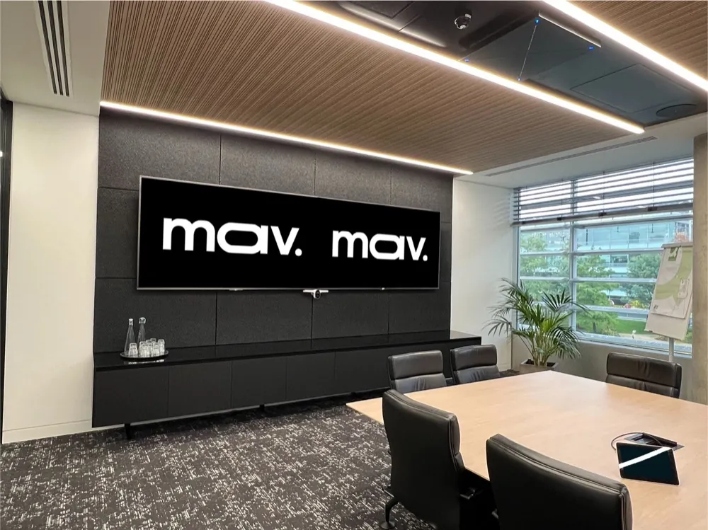 Boardroom with dual displays on a dark acoustic wall panel beneath a timber slat ceiling
